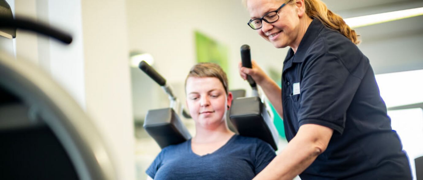 Therapeutin unterstützt Patientin der Physiotherapie an der Beinpresse