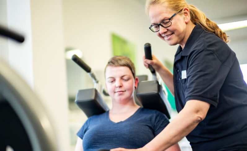 Therapeutin unterstützt Patientin der Physiotherapie an der Beinpresse