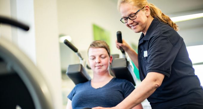 Therapeutin unterstützt Patientin der Physiotherapie an der Beinpresse