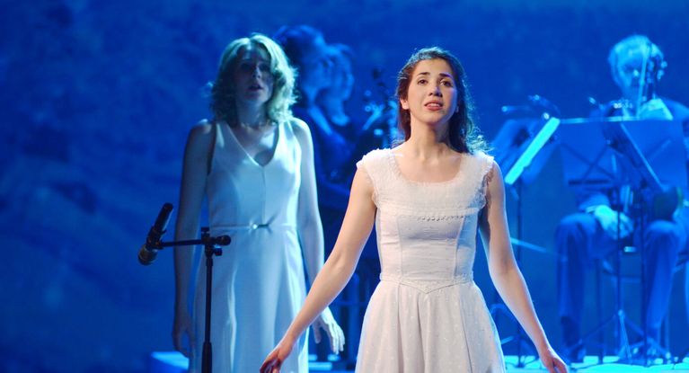 Junge Frau in weißem Kleid singt auf einer Bühne