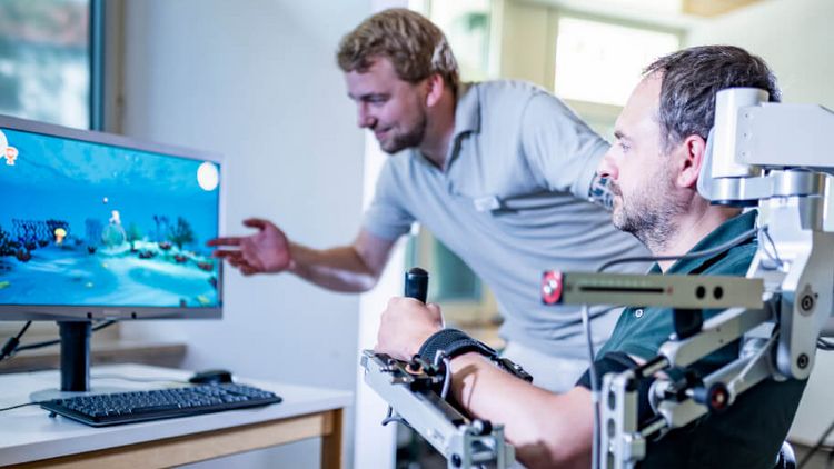 Therapeut erklärt Patienten Ergebnisse des Armtrainings mit Armeo auf einem Monitor