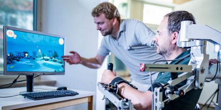 Motoriktraining Therapeut erklärt Patienten Ergebnisse des Armtrainings mit Armeo auf einem Monitor