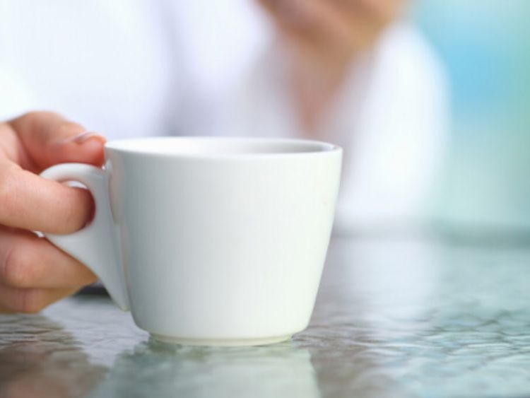 Frau hält eine Espressotasse in der Hand, auf dem Glastisch liegt ein Smartphone