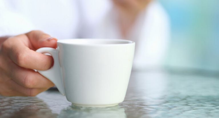 Große Aufmerksamkeit Frau hält eine Espressotasse in der Hand, auf dem Glastisch liegt ein Smartphone