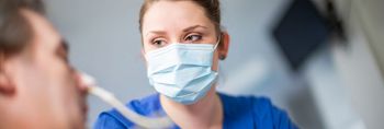 Pflegekraft mit Mundschutz schaut eine Patienten an, der eine Sauerstoffmaske trägt