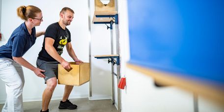 Patient hebt Kiste in der medizinisch-beruflich orientierten Rehabilitation
