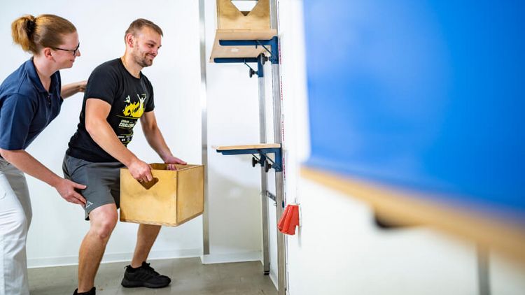 Patient hebt Kiste in der medizinisch-beruflich orientierten Rehabilitation