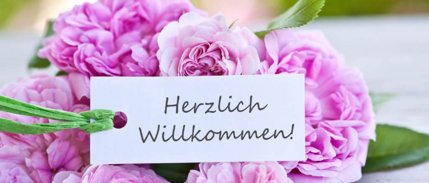 Pinkfarbene Blumen mit einem Herzlich Willkommen-Schild