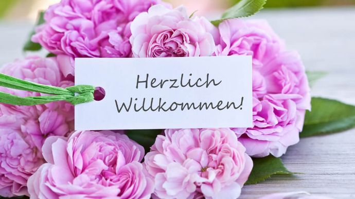 Pinkfarbene Blumen mit einem Herzlich Willkommen-Schild
