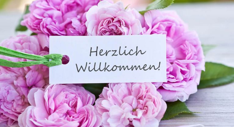 Pinkfarbene Blumen mit einem Herzlich Willkommen-Schild