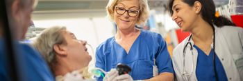 Ärztin und zwei Pflegekräfte sprechen mit einem im Bett liegenden Patienten
